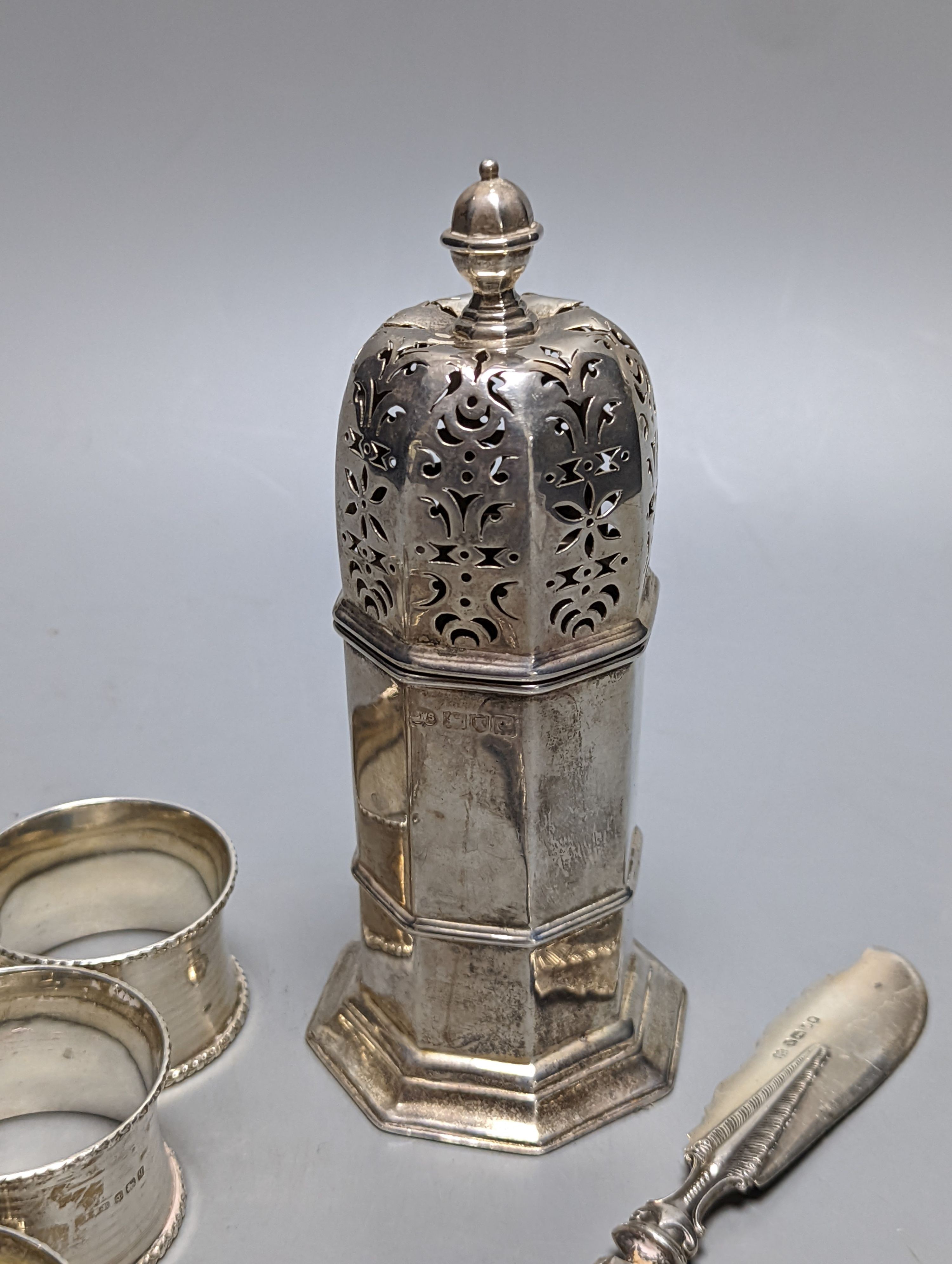 A set of six George V silver napkin rings, Birmingham, 1915, a silver sugar caster and silver butter knife.
